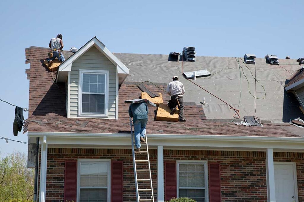 A roofer installing a black underlayment sheet over wooden roof decking on a house.