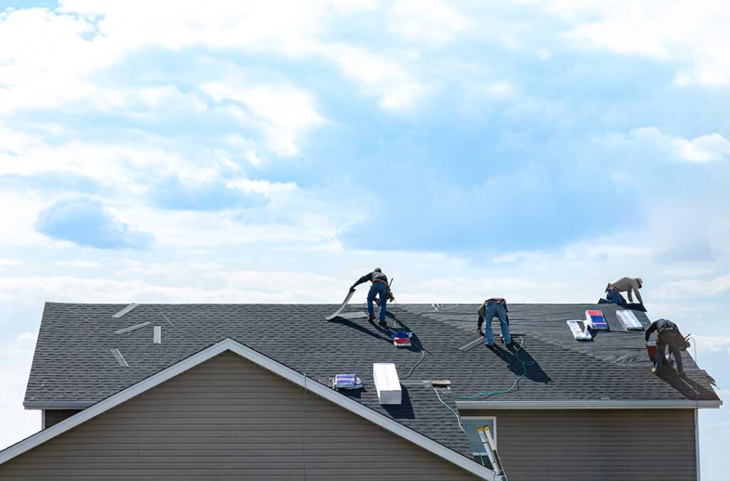 Homeowner checks roof shingles and cleared gutters beside a residential house in autumn.